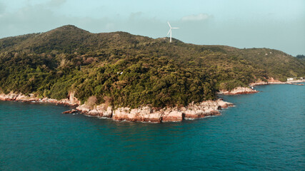 Mountains overgrown with greenery on the Lamma island and surrounded by the sea. There is a windmill at the top of the mountain. Hong Kong