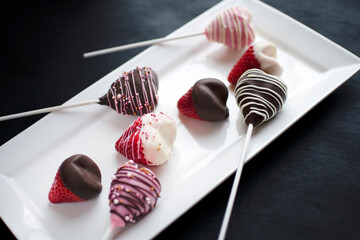 Heart Shape Strawberry Covered Chocolate Pops on White Plate on Black Background.