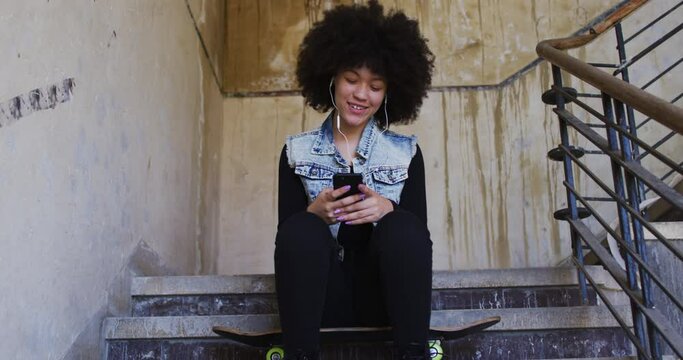 African american woman wearing earphones using listening to music while sitting on the stairs