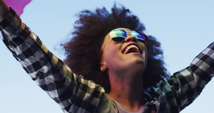 African american woman wearing sunglasses holding lbgt flag up in the air