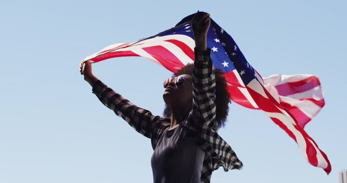 African american woman wearing sunglasses holding american flag up in the air