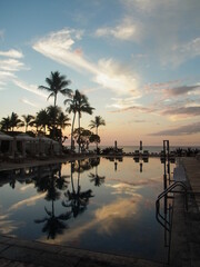 Beach, pool and palm trees in the beautiful sunset, sky  and clouds reflect in the pool