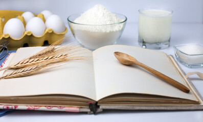 Blank cook book and baking ingredients: flour, eggs, milk and sugar. Cooking process. Close-up.