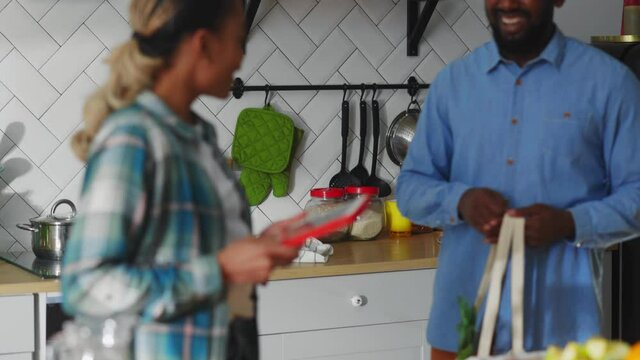Beautiful african young woman using tablet in her kitchen. Her hap py husband and son arriving home showing shopping bag full of healthy foods.
