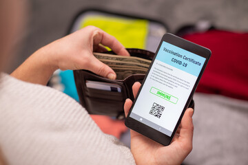 Traveller preparing for a trip, checking cash and looking to the phone with electronic copy of vaccination document. Vaccination certificate