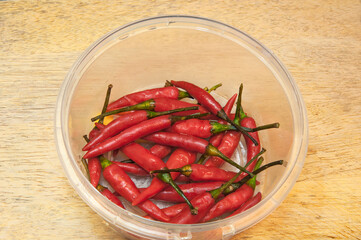 Red chili pepper in plastic container on a wooden background.
Top side view.