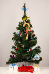 The Christmas tree is on the table, decorated with toys. There are gifts under it.