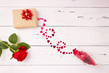 Red hearts spill out of a champagne glass, a gift box and a rose