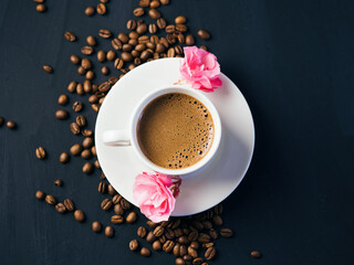 a cup of espresso coffee on a dark table top view. pink flowers buds