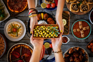Two women’s hands holding green marinated olive fruits in a bowl.