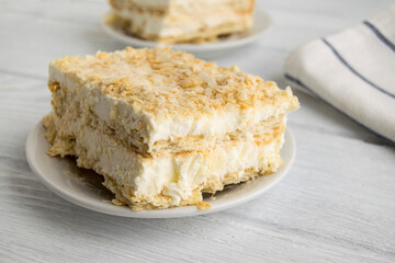 A piece of cake is on a white plate. Napoleon cake consists of ice cream, layered dough and biscuit crumbs. Сlose-up, wooden background.