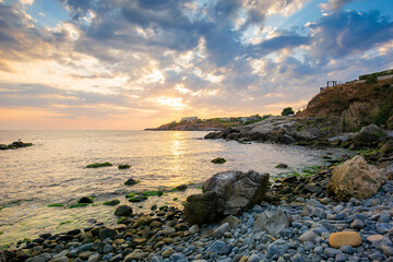 Fototapeta na wymiar dramatic sunrise at the sea. beautiful seascape with clouds on the sky above horizon. rocks and pebbles on the coast