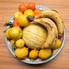 tray with fruit of lemons apples bananas tangerines oranges yellow melon kiwi on wooden table