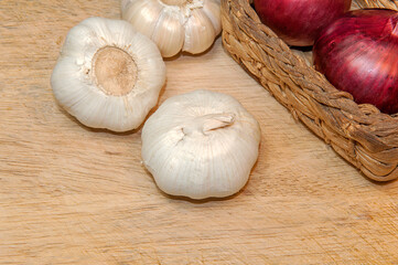 Organic garlic and red onion in wicker basket on light wooden table background with copy space for text, selective focus.
Top view.
