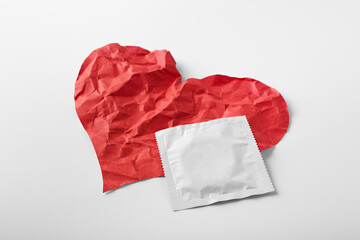 Condom with crumpled red heart shape paper isolated on white background. Valentine day, dating, make love concept. Contraception.