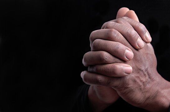 man praying to god with hands together on black background stock photo