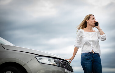 Pretty midle aged woman having car troubles - broken down car on the side of the road, calling the insurance company for assistance