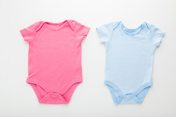 Pink and blue baby bodysuits on light gray table background. Closeup. Empty place for text or logo on apparel. Top down view.