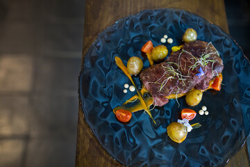 Plate of meat, tomatoes and potatoes on wooden table
