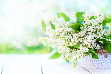 White lilac bouquet in basket on white wooden table and light background