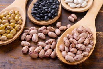 Assorted beans on spoons over wooden table