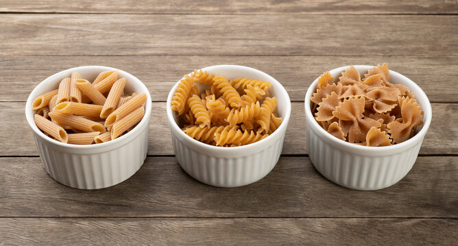 Assorted whole wheat pasta on bowls over wooden table