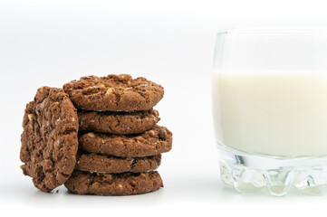 Stack of homemade sweet chocolate cookies with glass of milk on white.