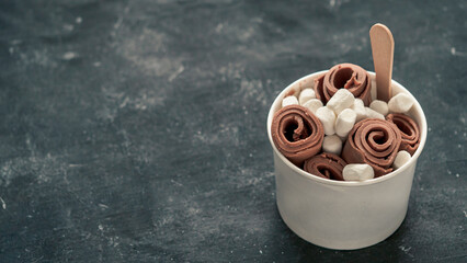 Rolled ice cream with in cone cup on dark rustic background. Iced rolls with chocolate. Thai style...