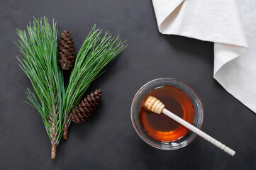 Pine honey in jar or bowl with honey stick and pine cones on rustic table, healthy food 