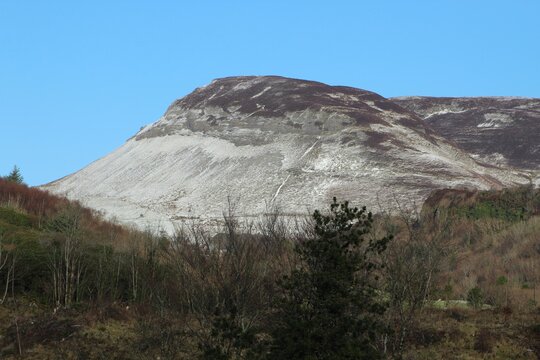 Snow-covered Keelogyboy Mountain against backdrop of blue sky with Deerpark forest in foreground. County Sligo, Ireland