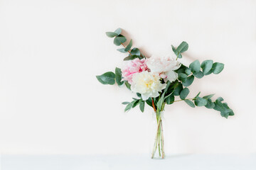 Bouquet of peonies with eucalyptus sprigs in glass bottle.