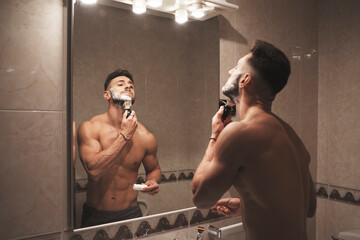 A strong and handsome boy rubs his face with a brush full of foam