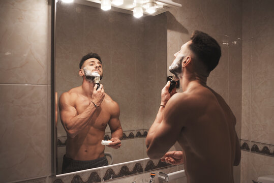 A strong and handsome boy rubs his face with a brush full of foam