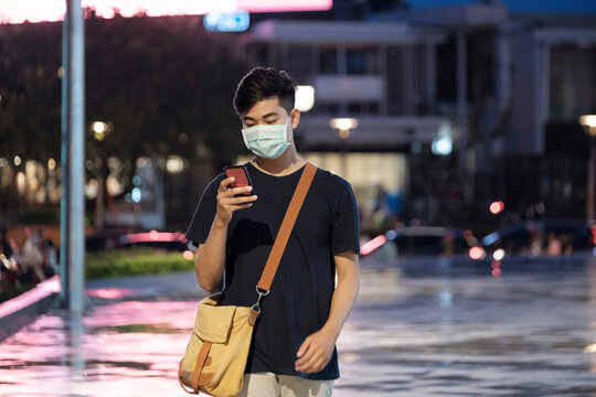 Young man with protective face mask using mobile phone in city s