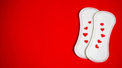 two white sanitary pads top view with red hearts symbolizing blood on a red background top view . feminine hygiene items
