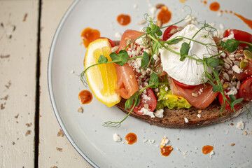 Smoked salmon and avocado on toast, topped with poached egg and dressing