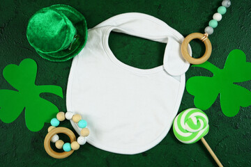 Happy St Patrick's Day baby wear white bib, styled with leprechaun hat, shamrocks, on a textured...