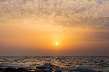 bright yellow-orange sunset over the sea against a blue sky with multicolored pink clouds and sun rays all over the sky