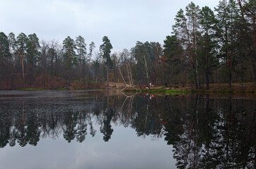 Obraz premium Cloudy autumn landscape. Scenic pond in the autumn colored forest. Trees reflected in the water. Autumn nature on the Pushcha-Vodytsia. Kyiv neighborhood, Ukraine