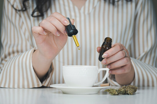 Close-up of female hand holding pipette with cbd oil, dripping into coffee mugs. Concepts of alternative medicine, natural pain reliever and herbs