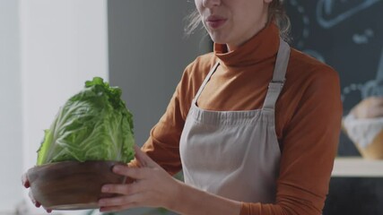 Young female chef in apron showing fresh napa cabbage and explaining recipe while filming online cooking class in kitchen