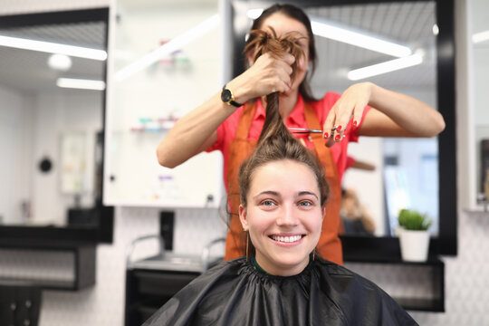 Portrait of smiling woman in hairdressing salon, which master cuts her hair. Women's haircuts and styling in a beauty salon concept