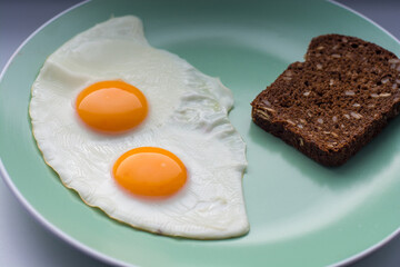 delicious breakfast two fried eggs  with bright yellow yolks on a green plate with a piece of black cereal bread