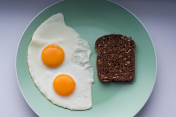 delicious breakfast two fried eggs  with bright yellow yolks on a green plate with a piece of black cereal bread