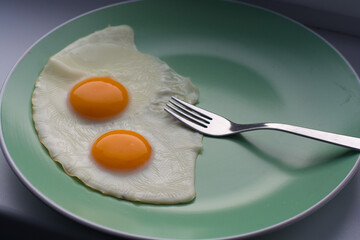 delicious breakfast two scrambled eggs with bright yellow yolks on a green plate and a silver fork