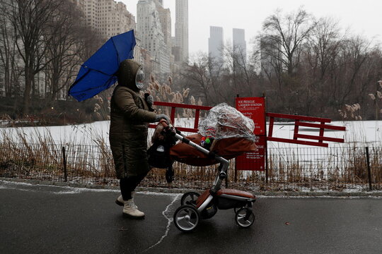 A woman carrying an umbrella pushes a baby stroller at Central Park as snow falls in New York