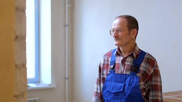 A middle aged construction worker wearing glasses a mustache and a uniform looks around the apartment