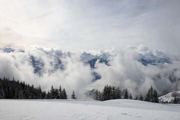 Winter landscape of a snowy mountain range with lingering clouds and a ski slope near Zell am See (Schmittenhöhe, Salzburg, Austria).