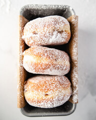 three sugared doughnuts filled with jam in a tray