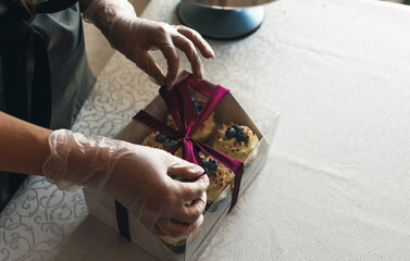 A girl cook in a gray apron packs cupcakes with cream in a gift box to send the order to the customer.